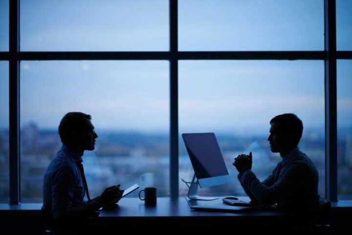 Two business professionals consulting at computer in modern office overlooking city representing digital strategy consultation