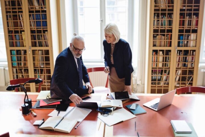 Two senior attorneys collaborating on legal documents in prestigious law library with extensive legal reference collection